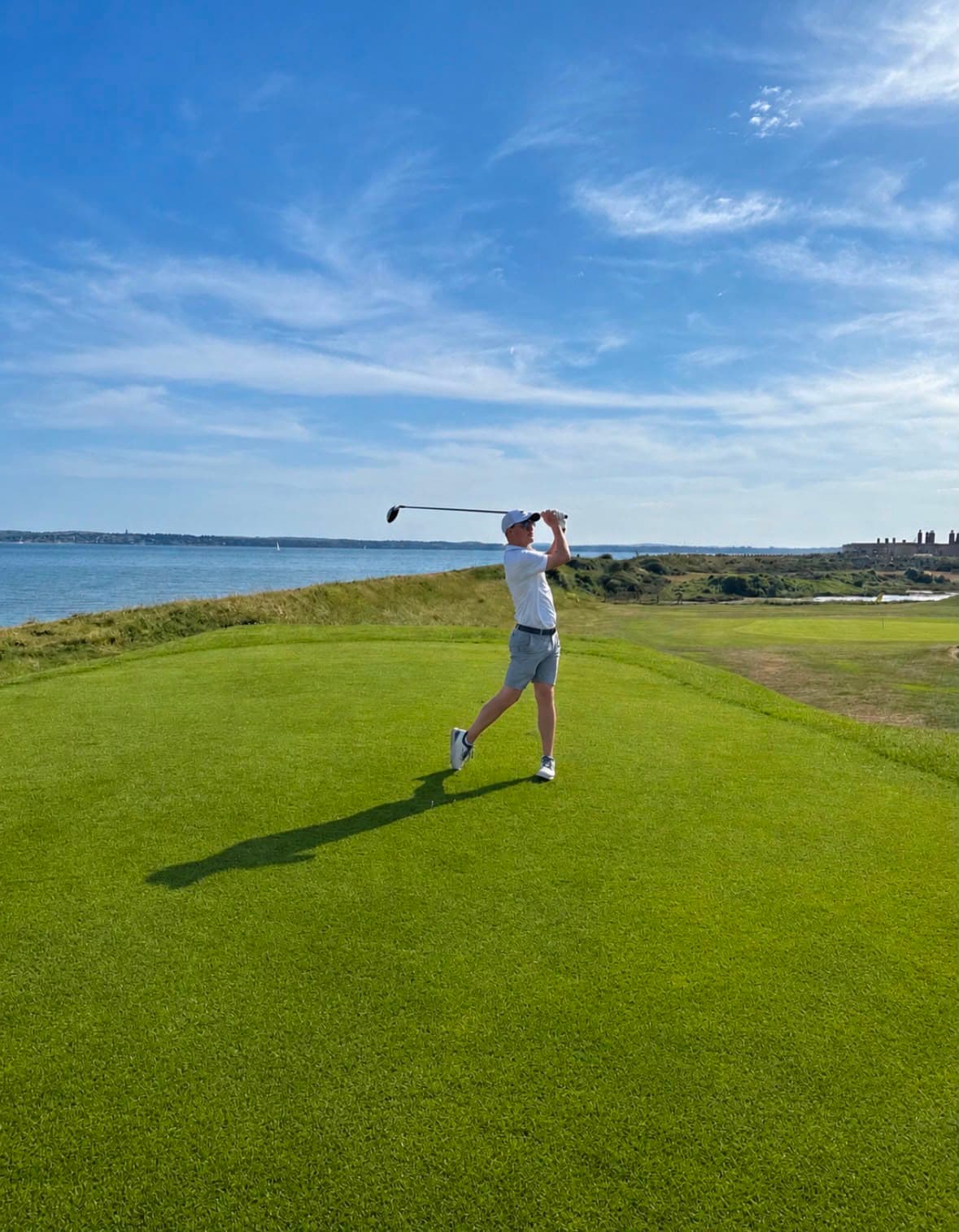 A golfer finishing a drive from an elevated tee, with the Solent and the Isle of Wight across the water behind