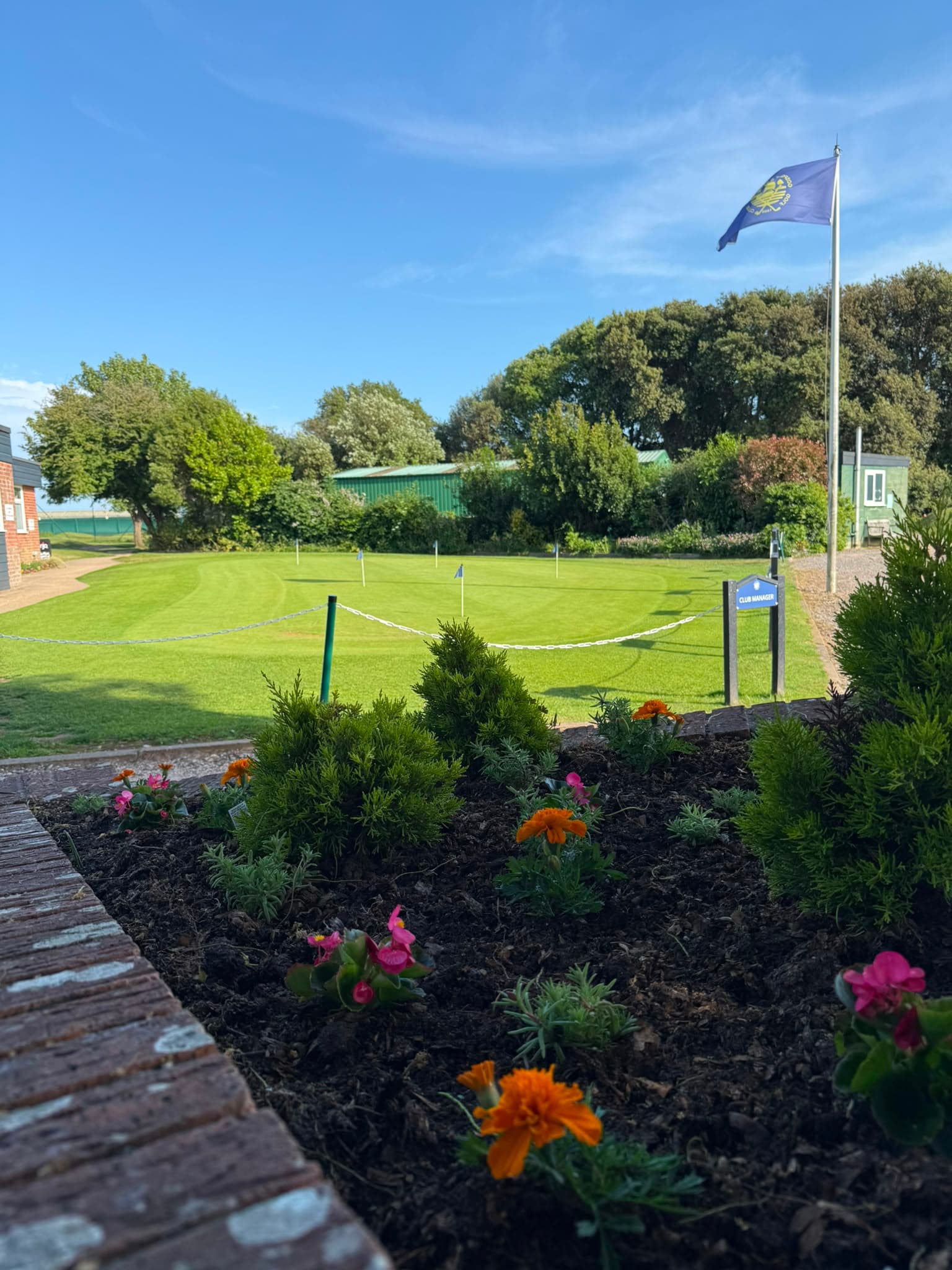 The practice green with the clubhouse flower beds in the foreground